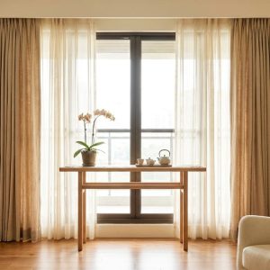 Living room with sheer beige curtains, a wooden table by a large window, an orchid plant, a teapot and cups, and a beige sofa on the right.