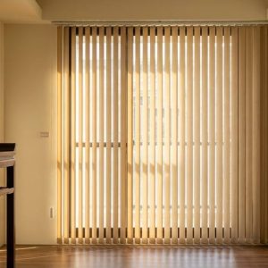 Sunlit minimalist living room with vertical blinds covering a large glass door and a dark wooden console on the left.