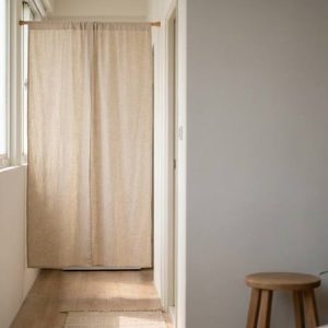 Beige curtain across a narrow sunlit hallway at the far end, with windows on the left and light wood flooring.