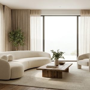Modern living room with a curved beige sofa, light armchair, and wooden coffee table on a large rug by floor-to-ceiling windows with beige curtains.