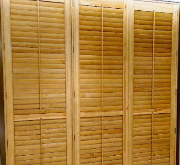 三片式的木質百葉折疊門或百葉窗特寫,葉片為水平設計,顏色是溫暖的淺棕色或原木色。葉片似乎處於關閉或部分開啟狀態