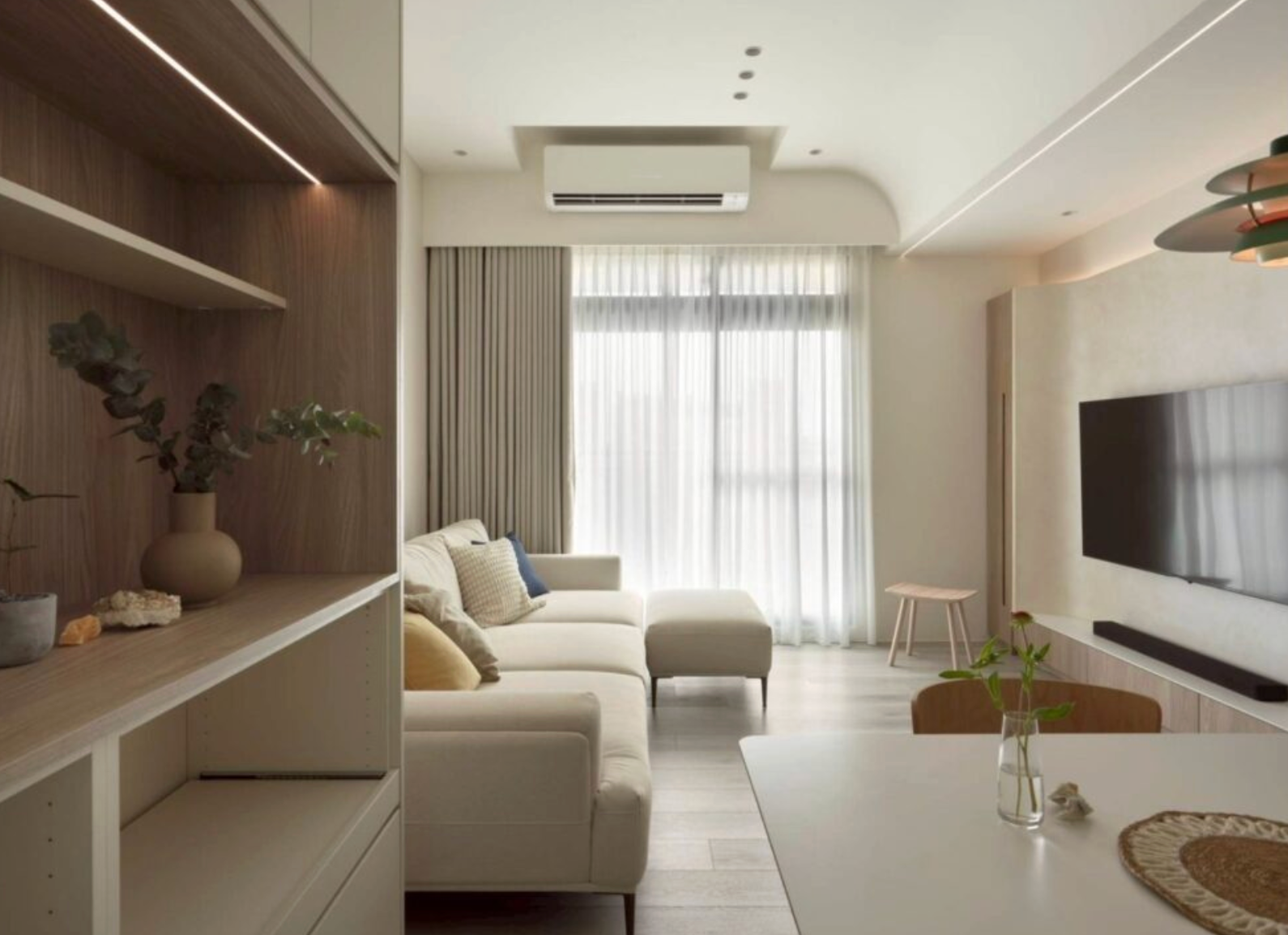 現代簡約風格客廳。落地窗戶上安裝了雙層窗簾:一層是淺米色厚布窗簾,一層是白色紗簾。中央米色沙發,天花板有分離式冷氣和崁燈。